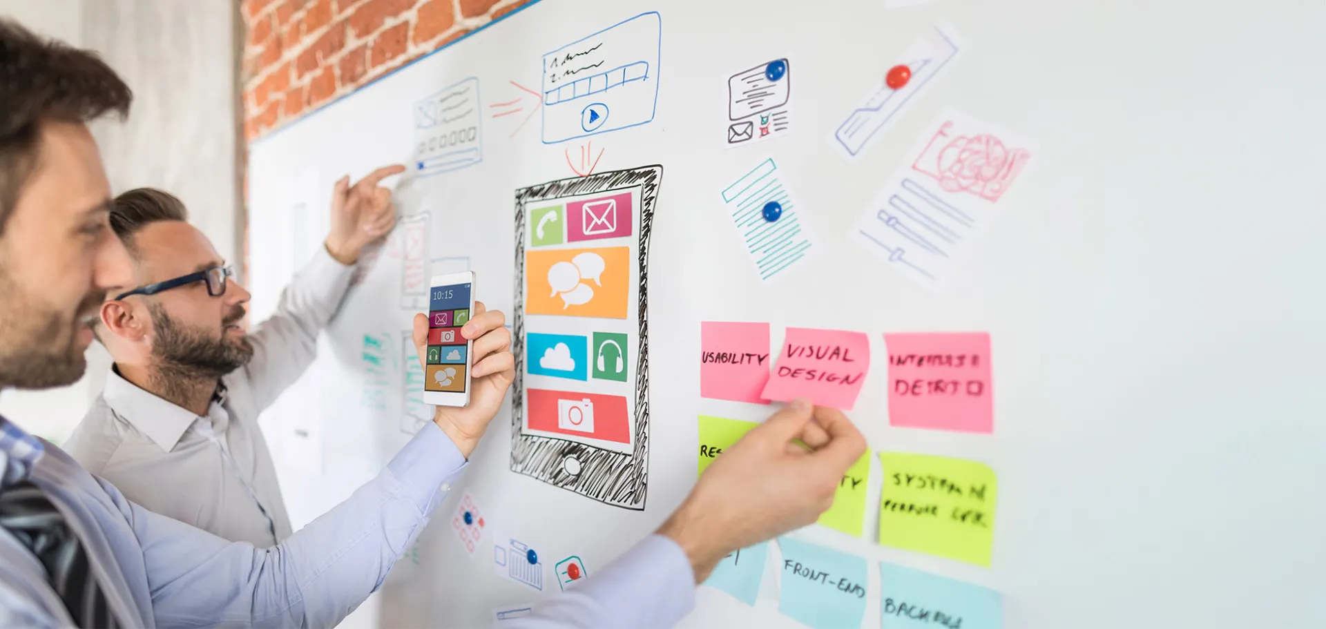 Two UX designers collaborate on a mobile app interface by sketching and organizing user interface elements on a whiteboard, highlighting usability and visual design.